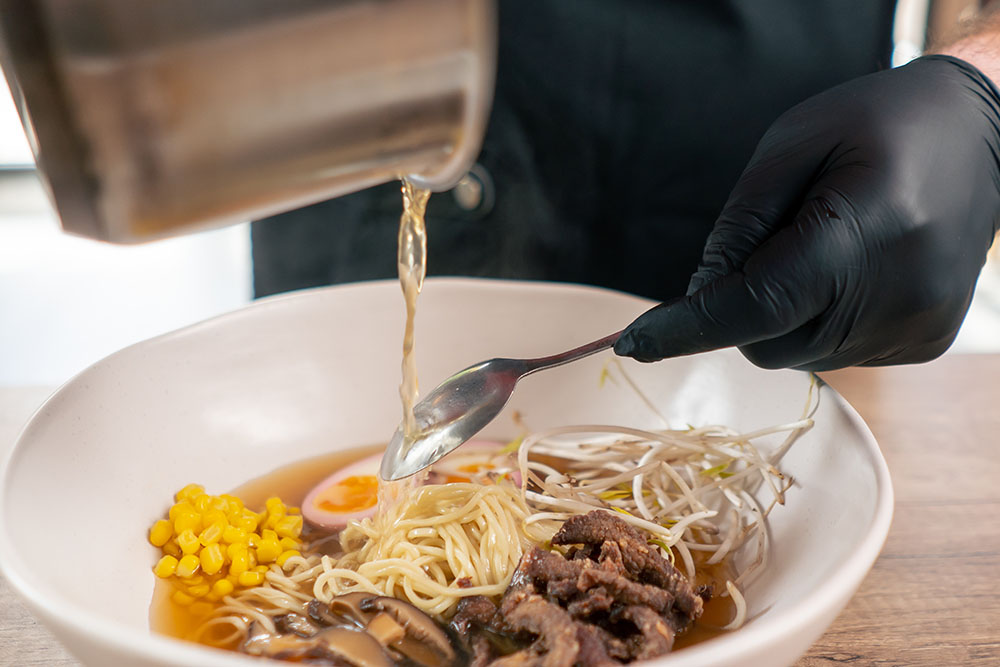 Vista de una persona añadiendo caldo en un tazón de ramen.