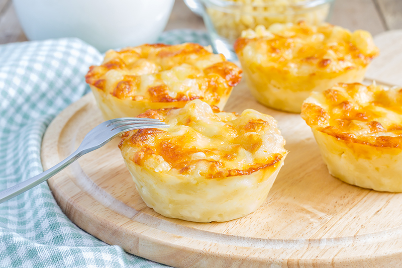 Macarrones con queso en forma de cupcakes con un tenedor sobre una superficie de madera.