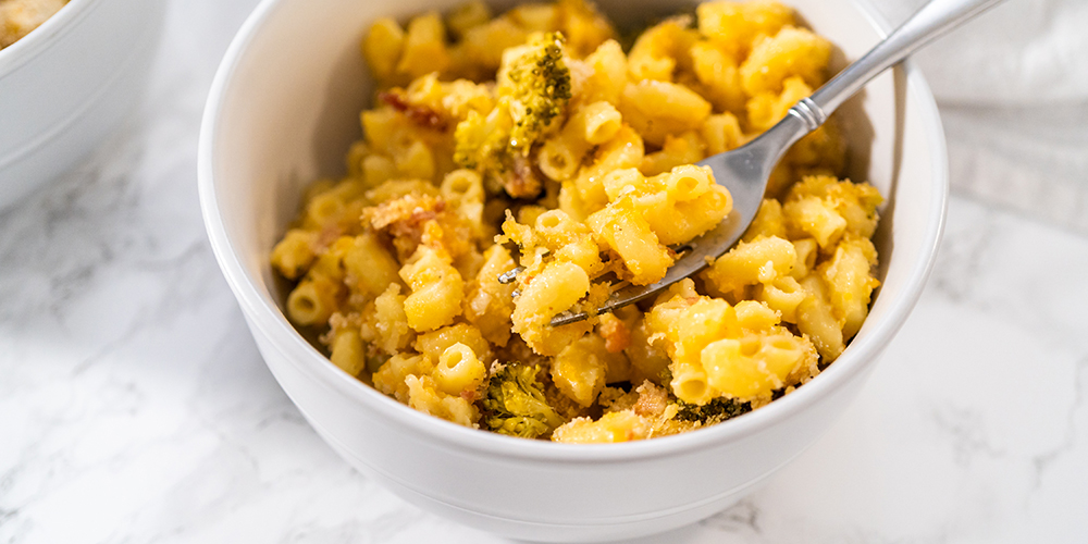 Macarrones con brócoli en un plato hondo con un tenedor sobre un fondo claro.
