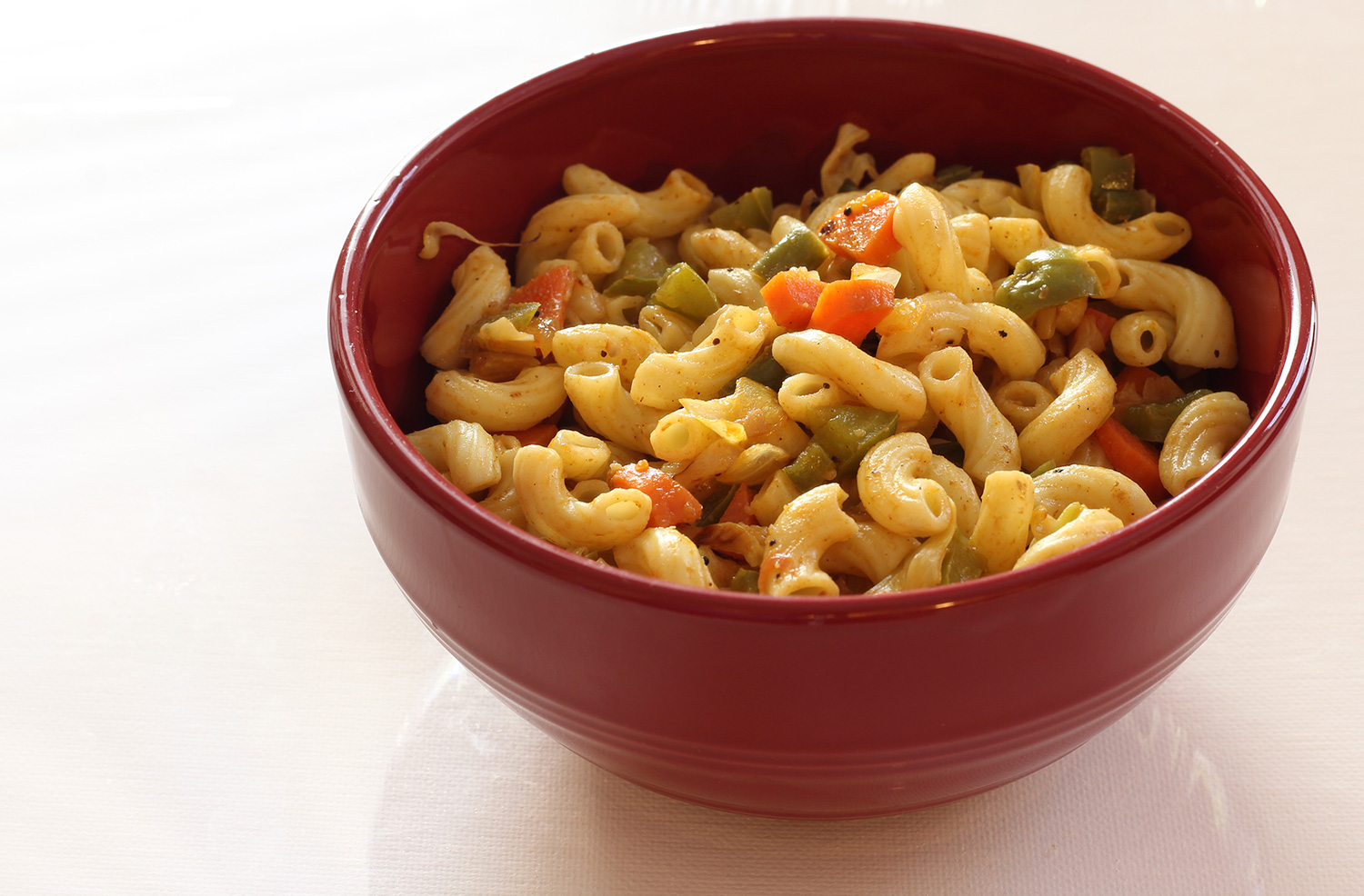 Macarrones con queso y vegetales en un plato rojo hondo sobre un fondo claro