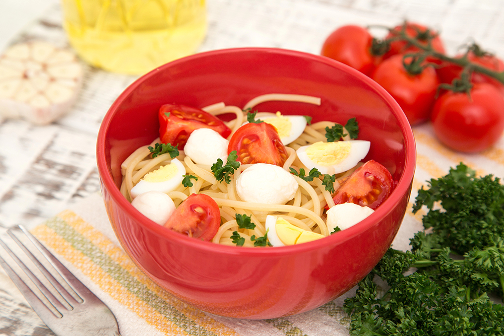 Pasta Spaghetti con pedazos de huevo cocido, tomate, todo sobre un plato rojo con decoración de perejil y tomates enteros en la mesa.